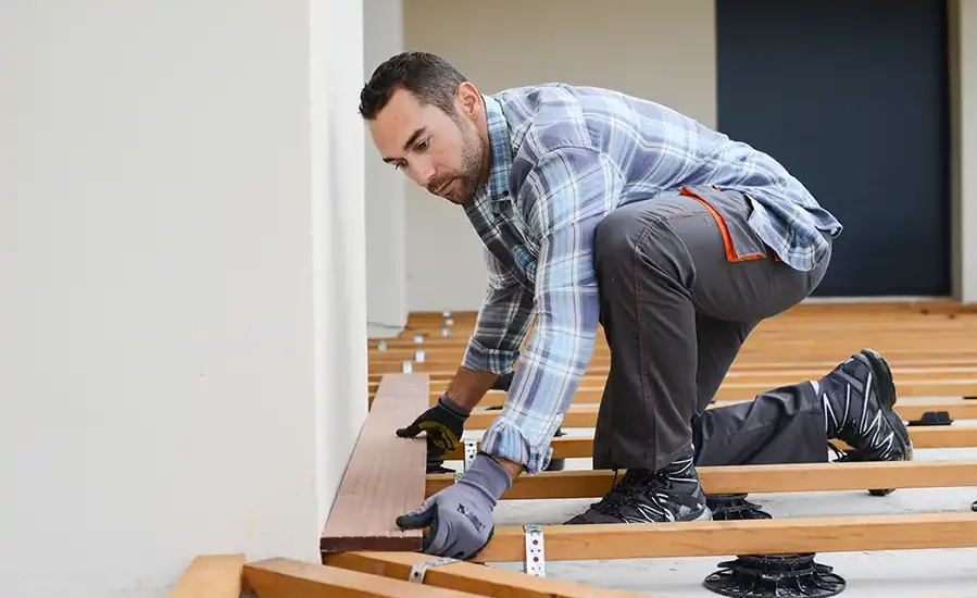 Deckbuilder holds board while kneeling on deck in progress
