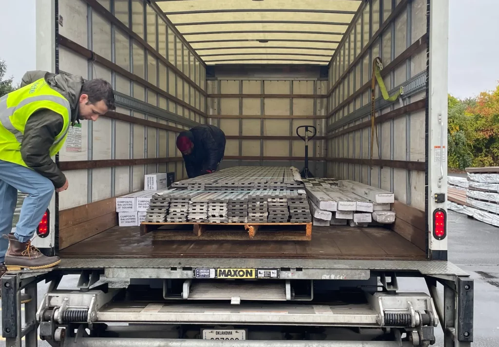 2 men load decking and other merchandise onto a delivery truck