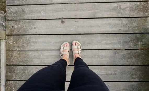 Feet in sandals looking down at weathered deck