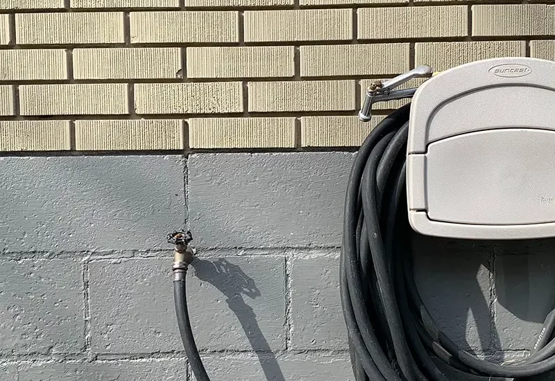 A coiled garden hose attached to spigot on brick foundational wall.