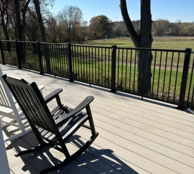 A sunny deck and railing with rocking chairs.