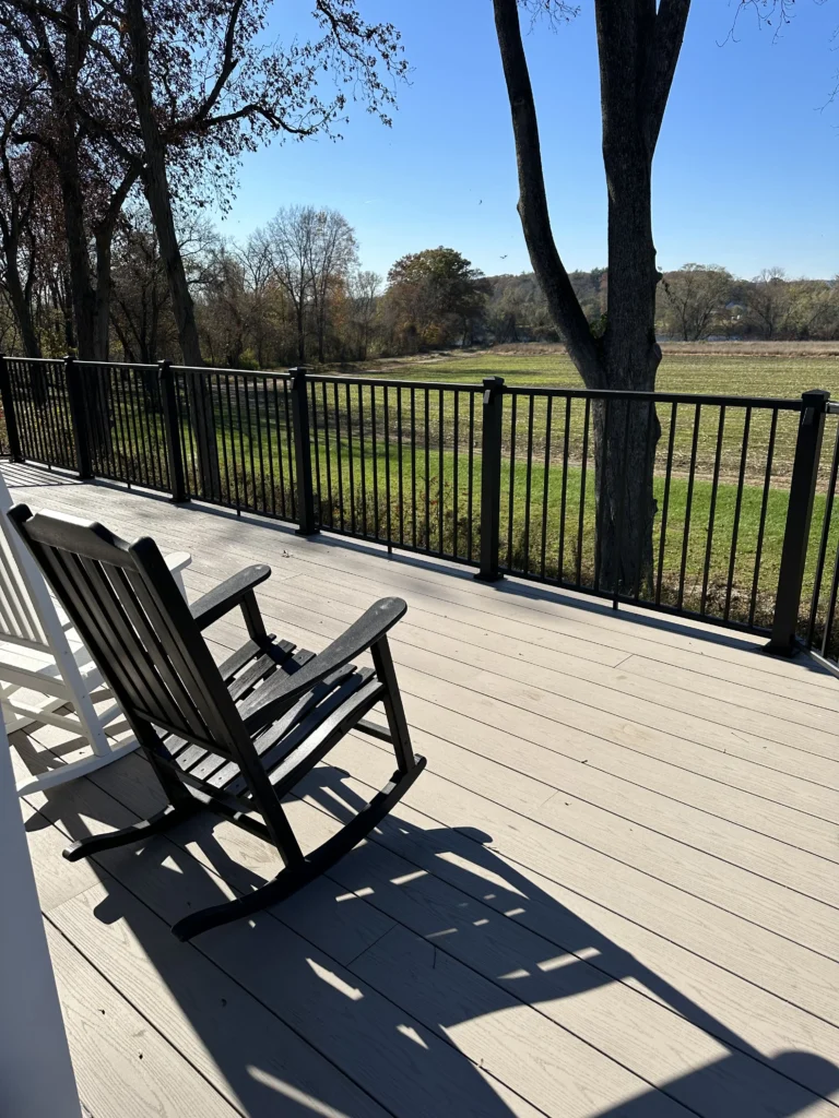 A sunny deck and railing with rocking chairs.