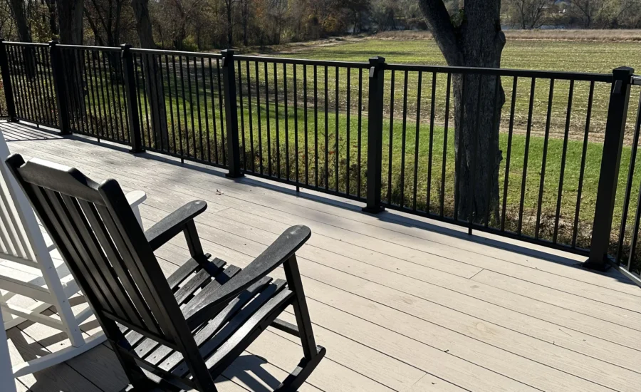 A sunny deck and railing with rocking chairs.