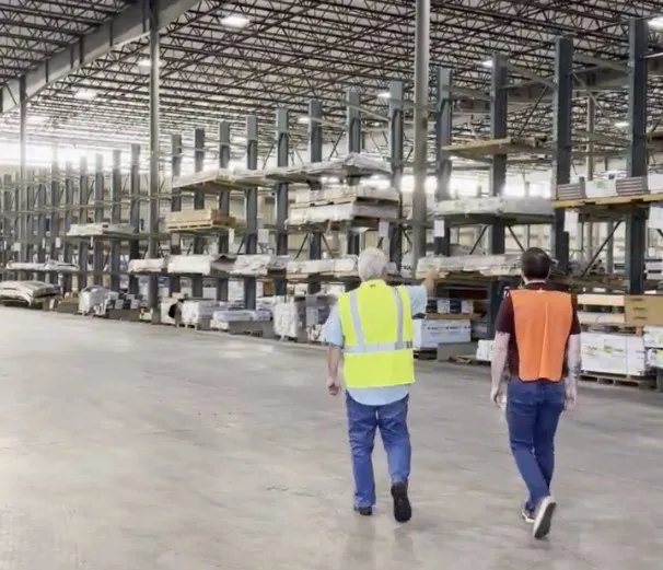 Two men in safety vests walking inside warehouse '71.