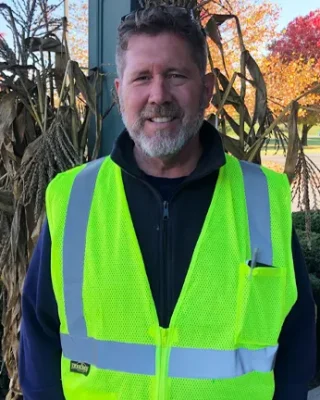 A man standing in front of foliage wearing a high-vis safety vest